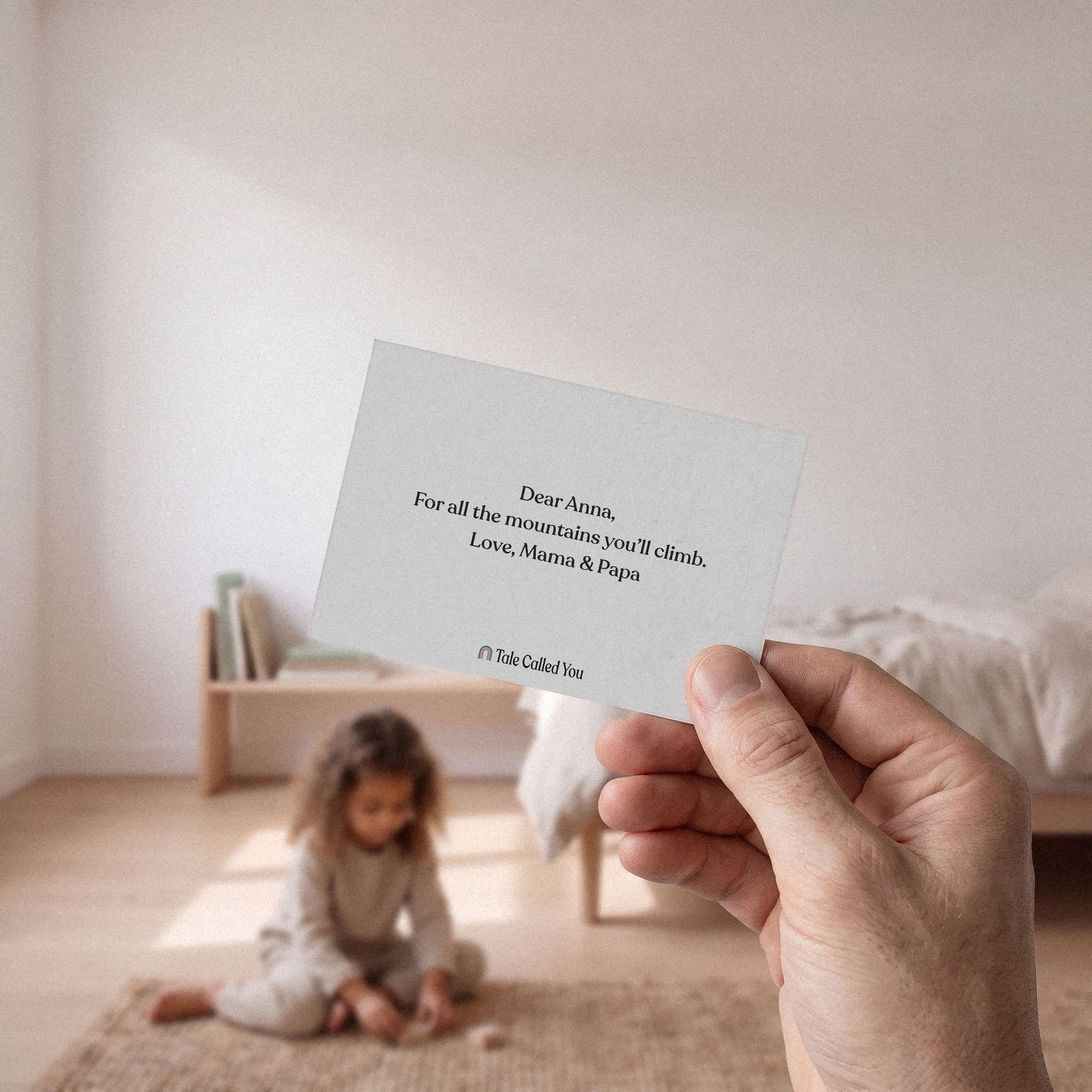 A hand holding the printed note card from the gift box, a child's room soft behind it